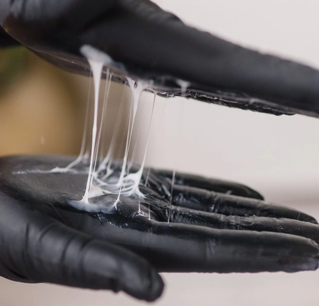 Black gloves stretching a white, stretchy substance against a neutral background